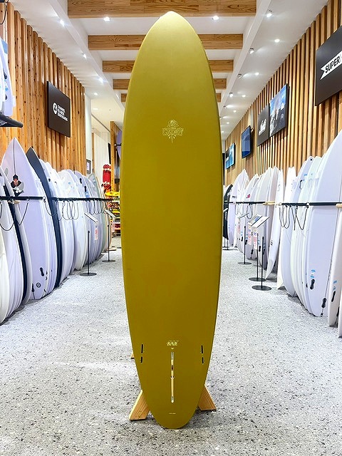 a-IMG_8672 - SHOP NEWS | ムラサキスポーツオンラインストア 通販 Yellow surfboard standing upright on a wooden display rack in a surf shop, surrounded by white boards on both sides