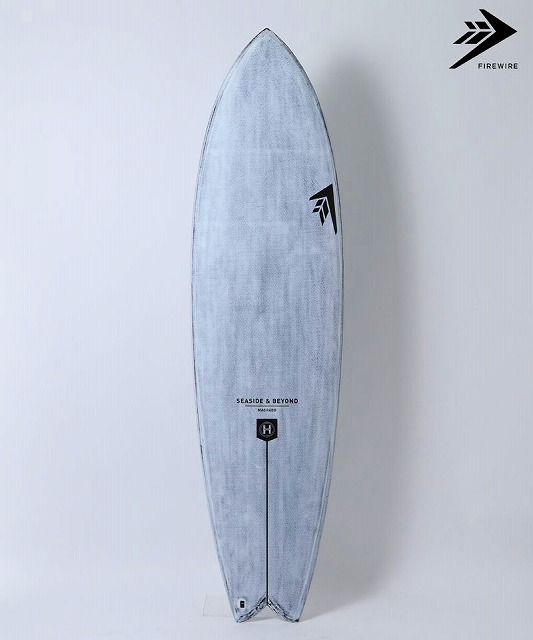 Light blue surfboard standing upright against a white background, with a black Firewire logo in the upper right and the branding 'SEASIDE & BEYOND' near the center.