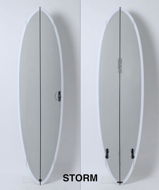 b-eMVGZbAg - SHOP NEWS | ムラサキスポーツオンラインストア 通販 Two pale gray surfboards with white rails stand upright against a white wall, center black stringer visible, STORM logo appears below.