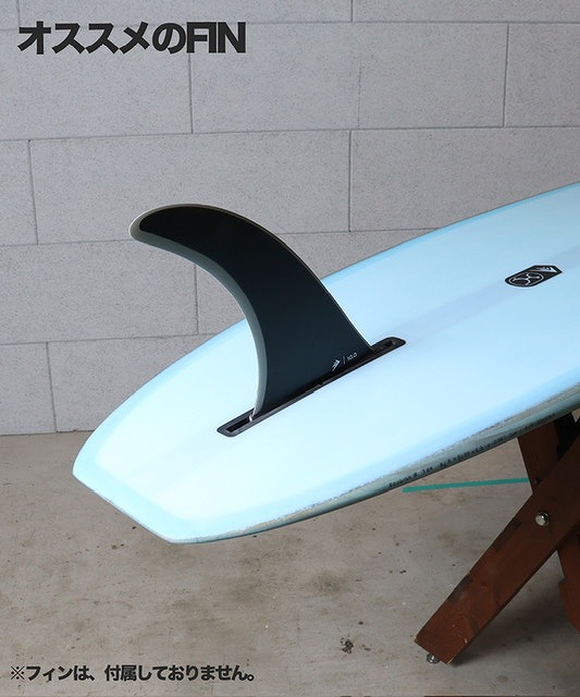 Light-blue shortboard with a black single fin mounted, resting on a wooden stand against a gray wall; Japanese title 'オススメのFIN' appears above.