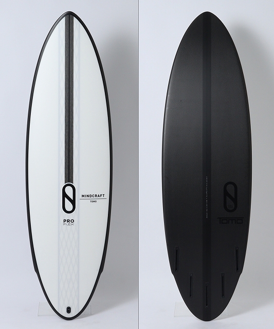 Two surfboards standing upright against a white wall: a white Mindcraft Pro Flex board on the left and a black Tomo board on the right.
