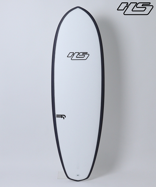 White surfboard with black edging standing upright against a light wall, featuring brand logos in the center and near the top.