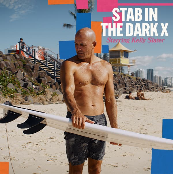 Promotional beach poster showing a shirtless man holding a surfboard, with colorful signs and the text 'STAB IN THE DARK X' starring Kelly Slater.