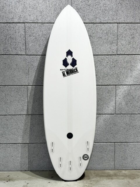 IMG_2861 - SHOP NEWS | ムラサキスポーツオンラインストア 通販 White surfboard standing upright against a gray concrete wall, featuring an Al Merrick logo and multiple fin boxes along the bottom.