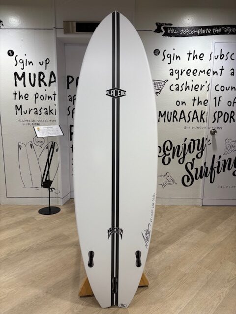 White surfboard with a double black stripe down the center, standing on a wooden display stand in a surf shop showroom.
