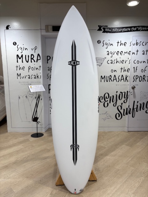 White surfboard with a vertical black pinstripe and emblem, displayed upright on a wooden stand in a showroom setting.