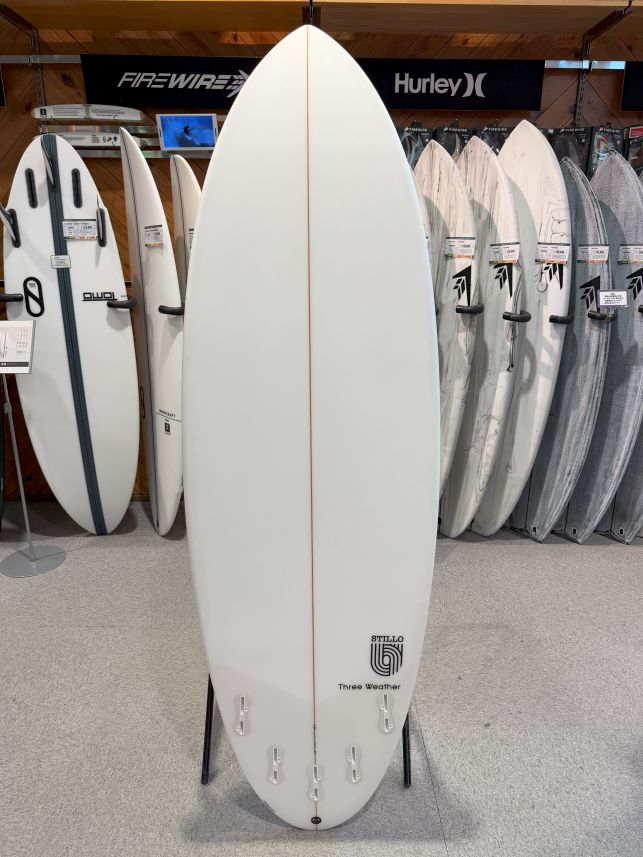 IMG_8603 - SHOP NEWS | ムラサキスポーツオンラインストア 通販 White surfboard on a stand in a surf shop, with other boards displayed behind it.