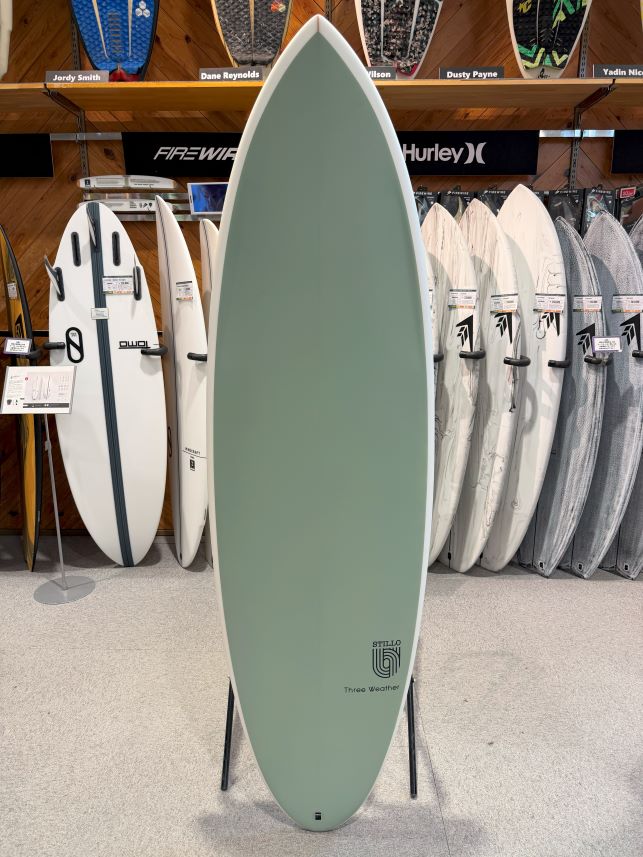 IMG_8605 - SHOP NEWS | ムラサキスポーツオンラインストア 通販 Mint green surfboard on a display rack in a shop, with white and gray boards lined up behind it.