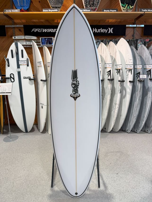 White surfboard on a stand in a surf shop, centered with other boards on racks behind and a logo in the middle