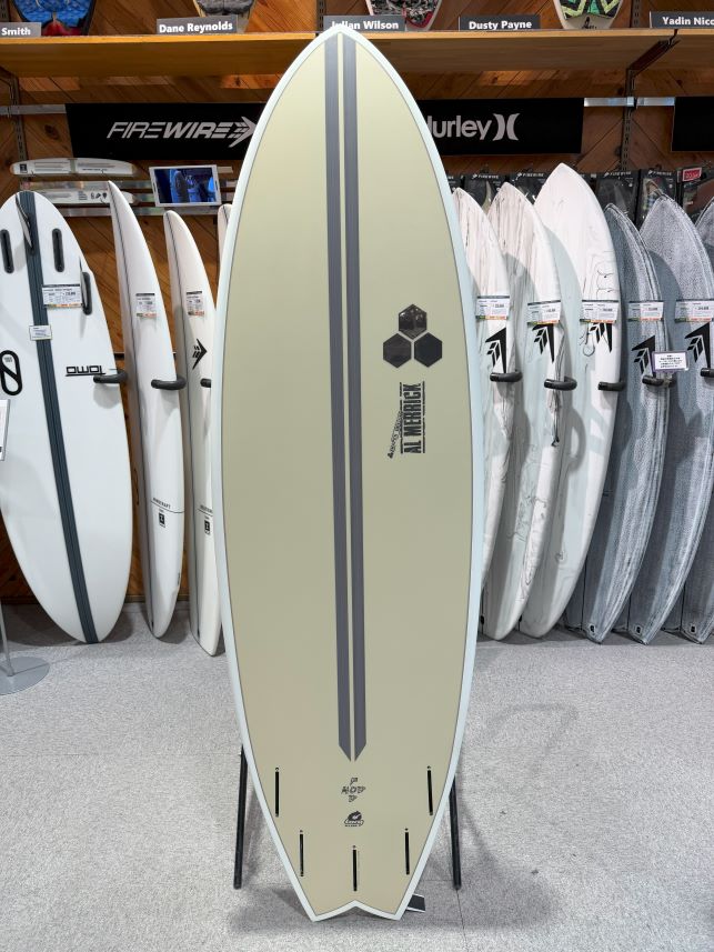 Beige surfboard with two dark center stripes on a display rack in a surf shop.