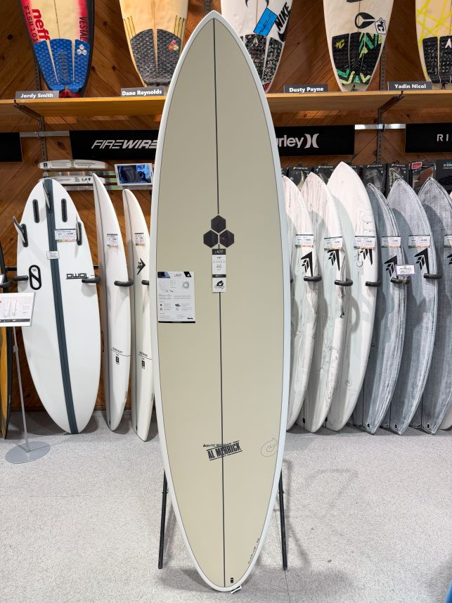 Cream-colored surfboard on a stand in a shop, with other boards on racks behind it.
