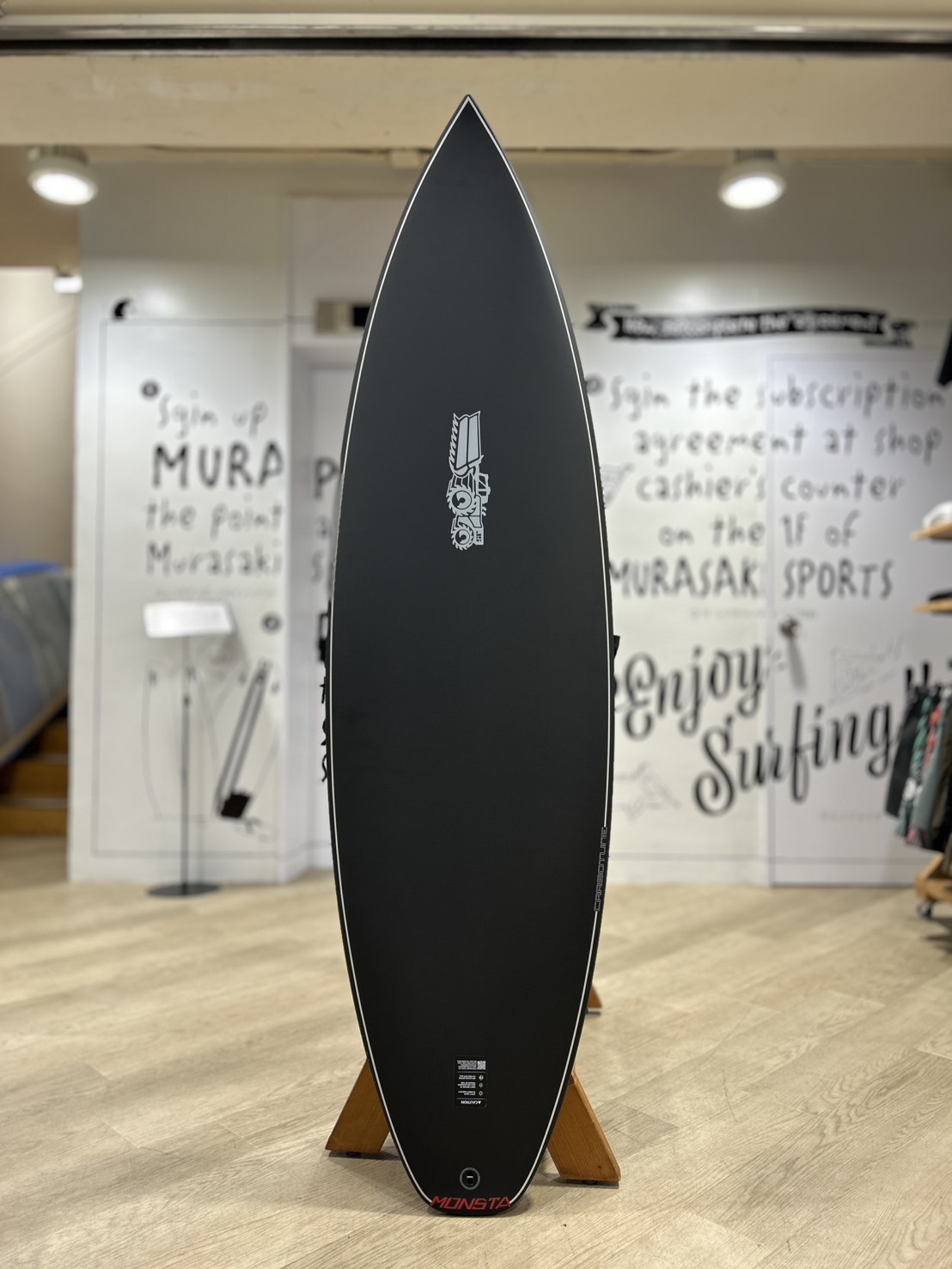 Black surfboard on a wooden stand inside a surf shop showroom.