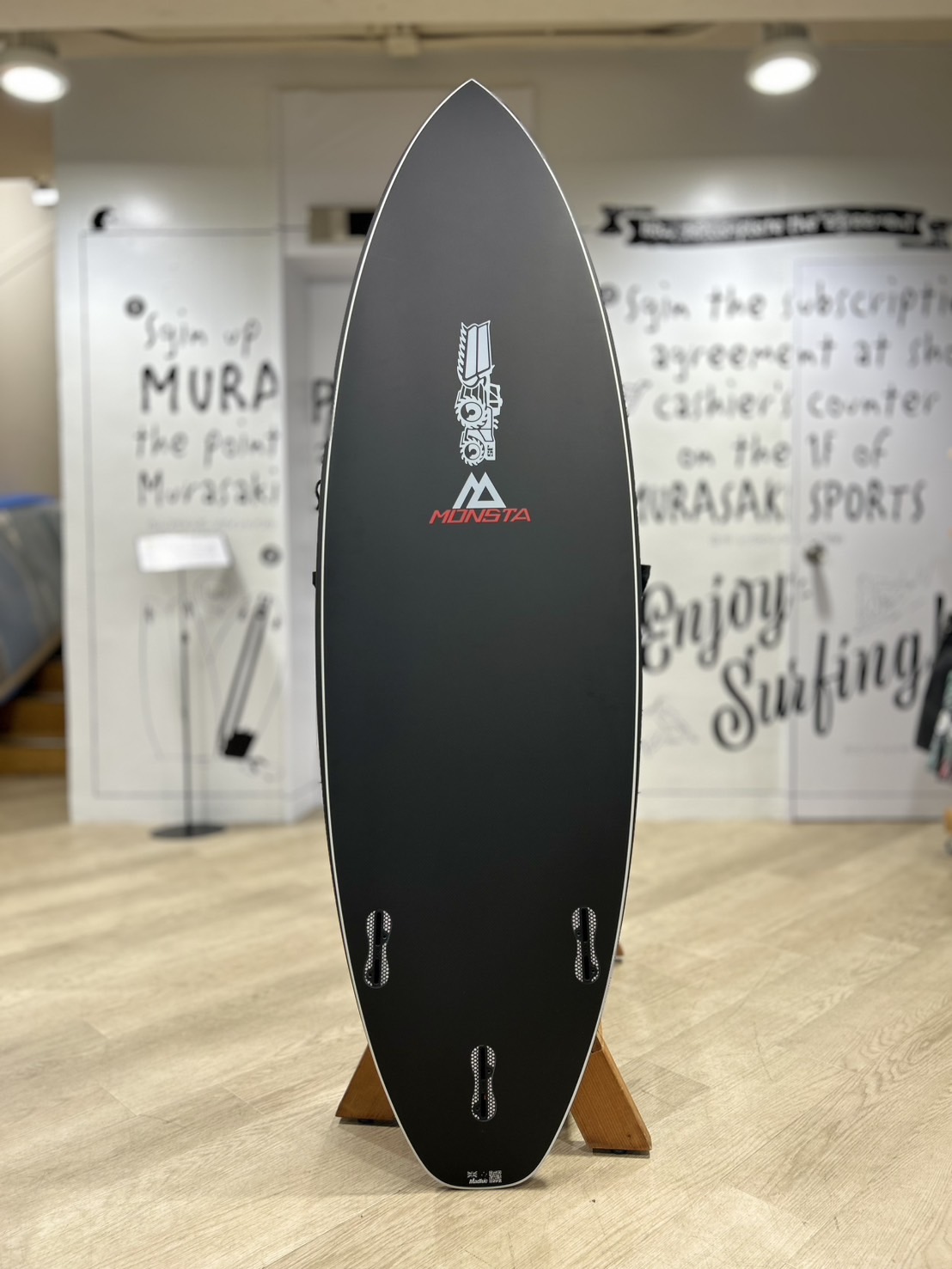 Black snowboard standing upright on a wooden rack in a showroom, Munsta logo visible on the board.