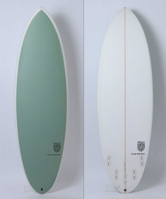 a-5Z9eluyw - SHOP NEWS | ムラサキスポーツオンラインストア 通販 Two surfboards standing upright side by side against a pale wall: left green board with white border, right white board with an orange stringer and multiple fins on the bottom edge.