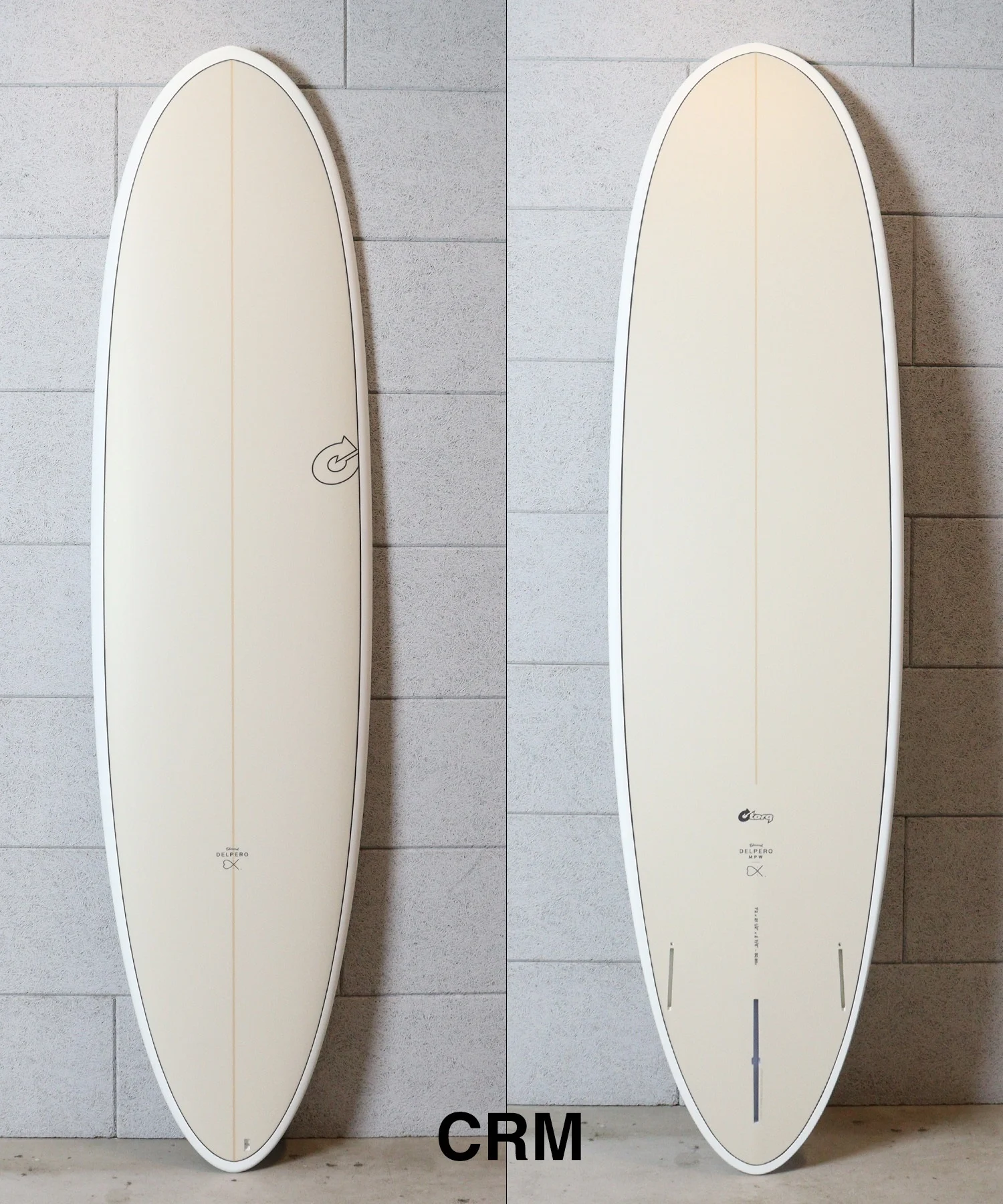 Two cream surfboards standing upright side by side against a tiled wall, each with subtle branding near the bottom (left board shows a circular logo).
