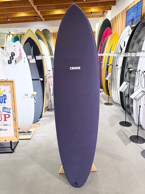 Purple surfboard on display rack in a shop, with 'CRIME' logo on the board and other boards in the background.