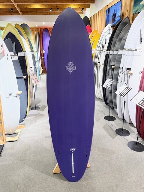 Purple longboard surfboard on a stand in a showroom, surrounded by colorful boards