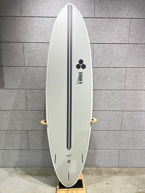 White surfboard with two black parallel stripes and a hexagon logo leaning against a gray brick wall, mounted on a wooden stand.