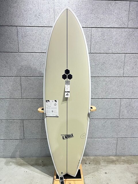 Cream surfboard on a wooden stand against a gray tile wall, with a black hexagon logo and attached price tags as signs of display accessory details.