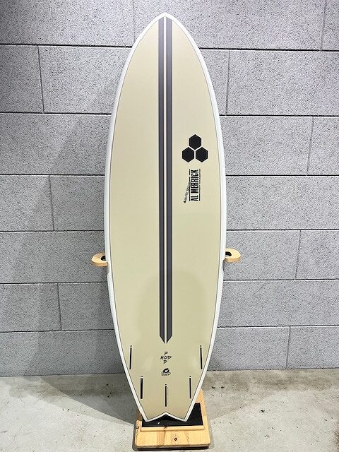 Cream-colored surfboard with two black vertical stripes standing upright on a wooden rack against a gray brick wall; visible logos near the center.