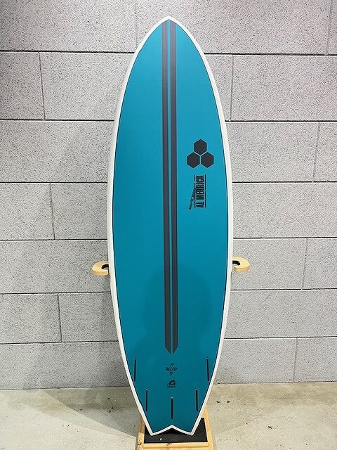 Blue surfboard with white edge standing upright against a gray cinder block wall, featuring two dark blue stripes and a hex logo.
