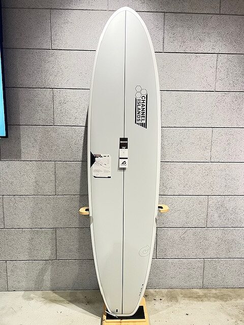 White surfboard standing upright on a wooden display rack indoors, with price tag and product labels attached to it.