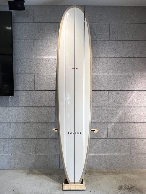 White surfboard with three thin dark stripes, standing upright on a wooden rack against a gray brick wall.