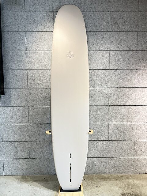 White longboard standing upright on a small wooden stand against a gray brick wall, indoors.