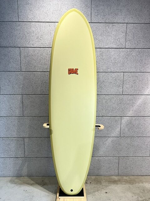 Yellow surfboard with a red logo stands upright against a gray tile wall on a stand.