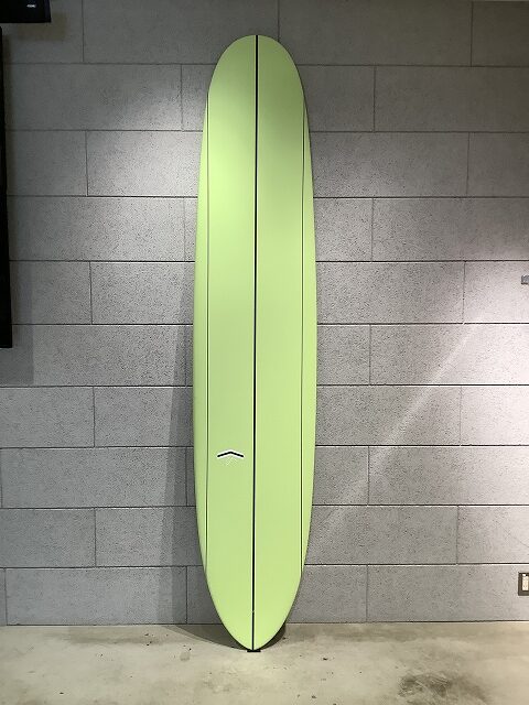 Neon green surfboard standing upright against a gray tiled wall indoors.