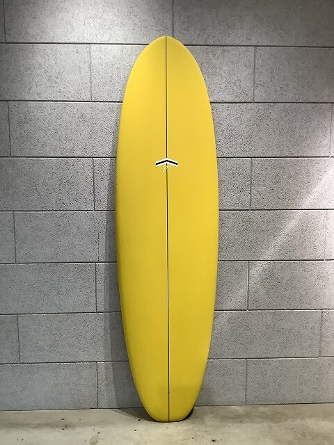 Yellow surfboard standing upright against a gray cinder-block wall.