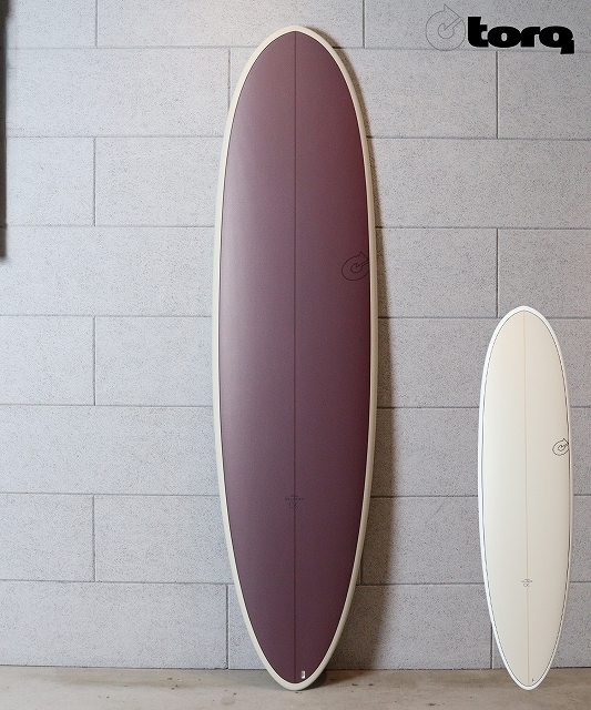 Two surfboards leaning against a gray block wall: a large burgundy board on the left and a smaller white board on the right (Torq logo in the top-right).