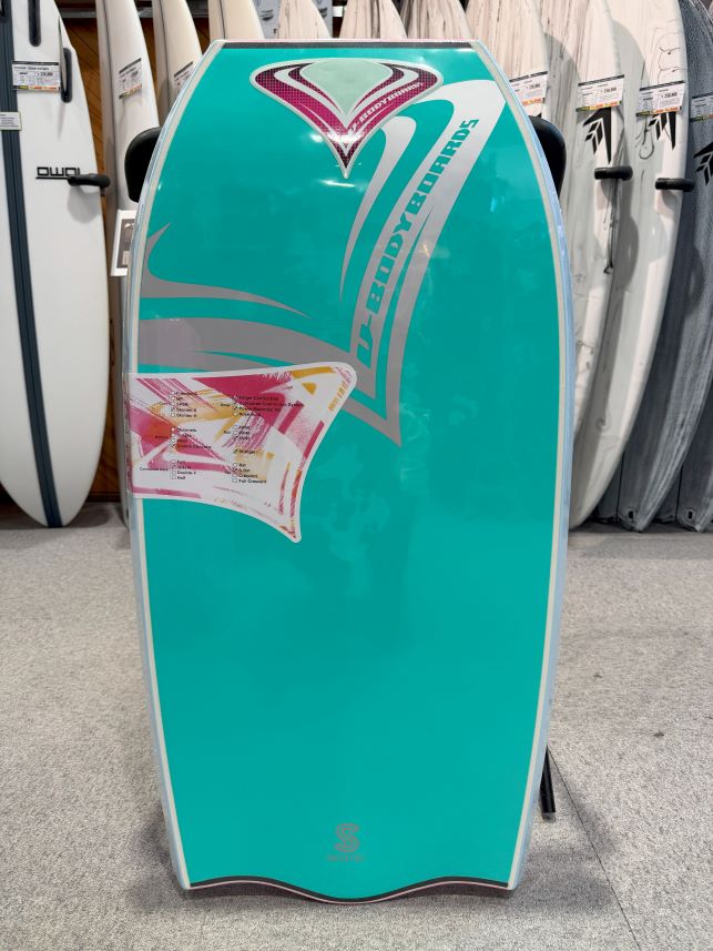 Turquoise stand-up paddleboard on display with bold teal and pink graphics and the brand name Liquid Force visible vertically on the side, in a shop setting.