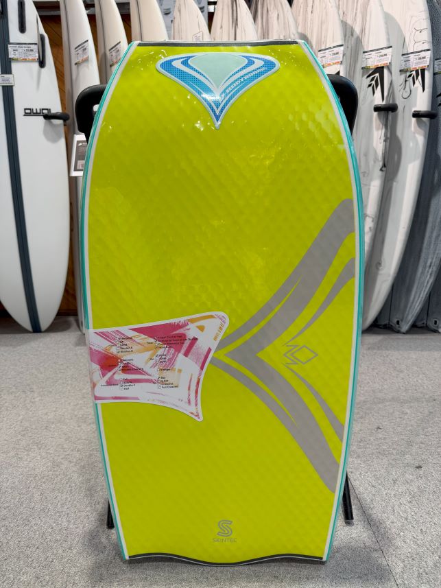 Bright lime-green wakeboard on display, turquoise edge, blue crest logo at top, with gray abstract graphics and other boards visible in the background.