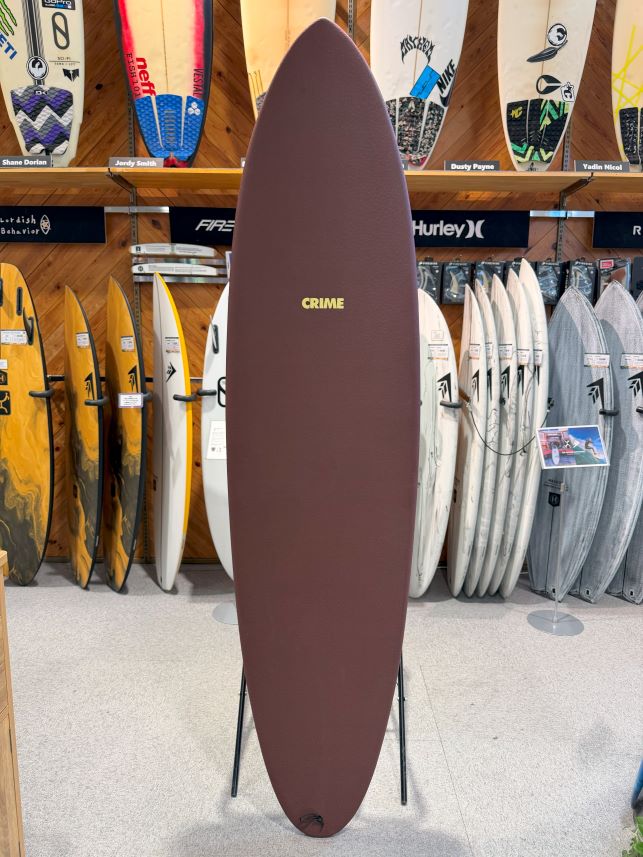 Maroon surfboard on a stand in a store, with a yellow 'CRIME' logo on the board's center