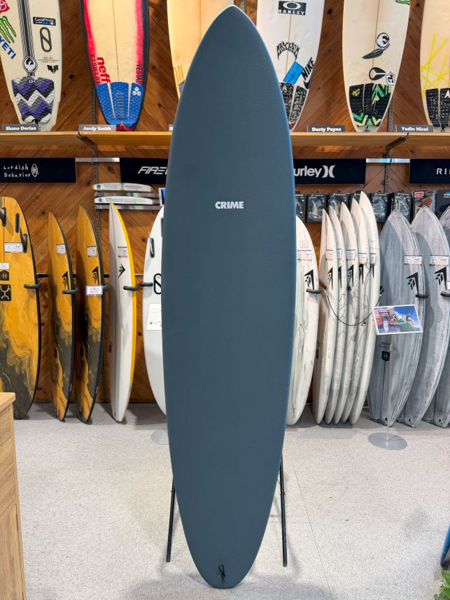 Blue surfboard on a display stand in a surf shop, labeled CRIME, with rows of boards visible in the background.