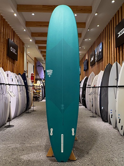 Teal surfboard on a display rack in a surf shop, surrounded by other boards on both sides.