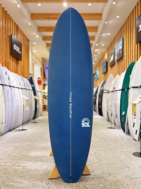 Blue surfboard on display in a shop, centered between rows of other boards with wooden walls behind it.