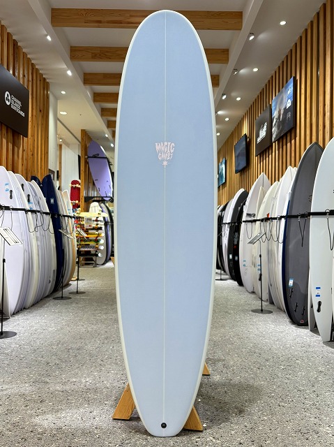 Light blue surfboard standing upright on display rack in a surf shop showroom.