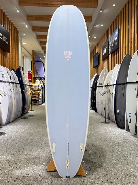 Light blue surfboard standing upright on a wooden display in a surf shop showroom.