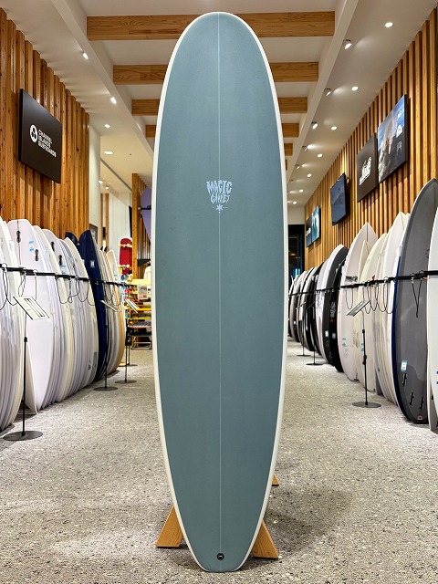 Teal surfboard on a wooden stand in a showroom, surrounded by other boards on racks.