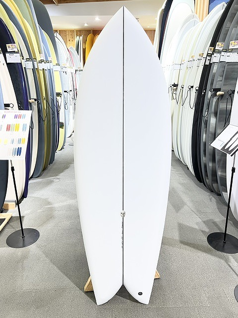 White twin-fin surfboard standing upright on display rack in a surf shop showroom.
