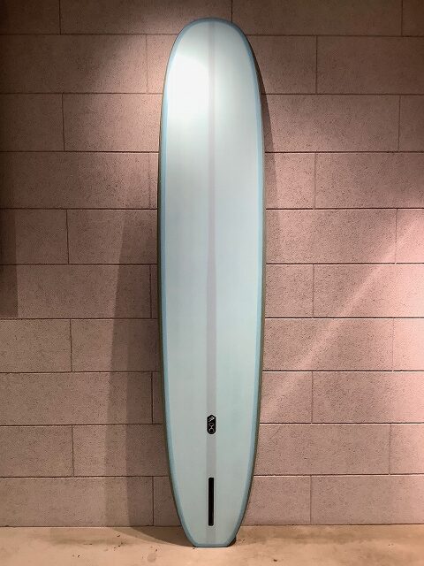 Pale blue surfboard leaning upright against a brick wall indoors.