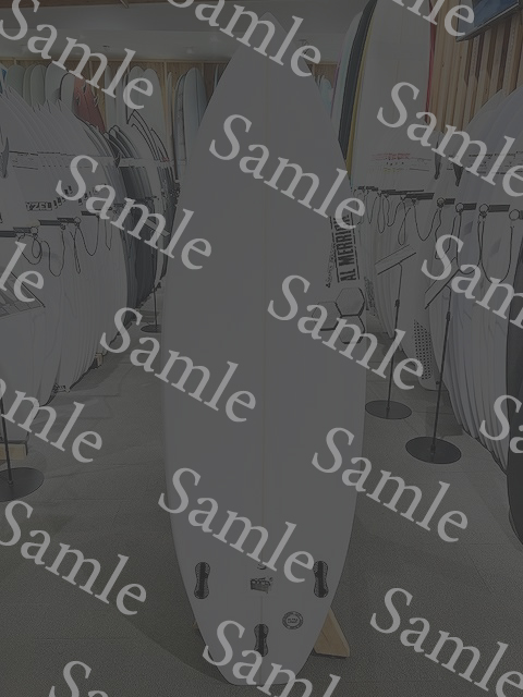 White surfboard standing upright in a showroom with rows of boards on racks in the background.