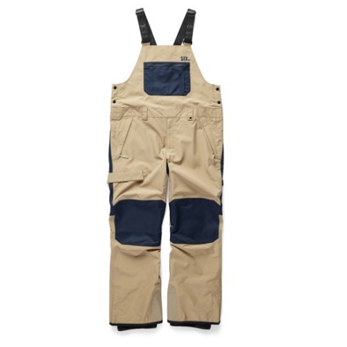 Tan bib overalls with navy knee patches and a blue chest pocket; black adjustable straps, casual workwear.