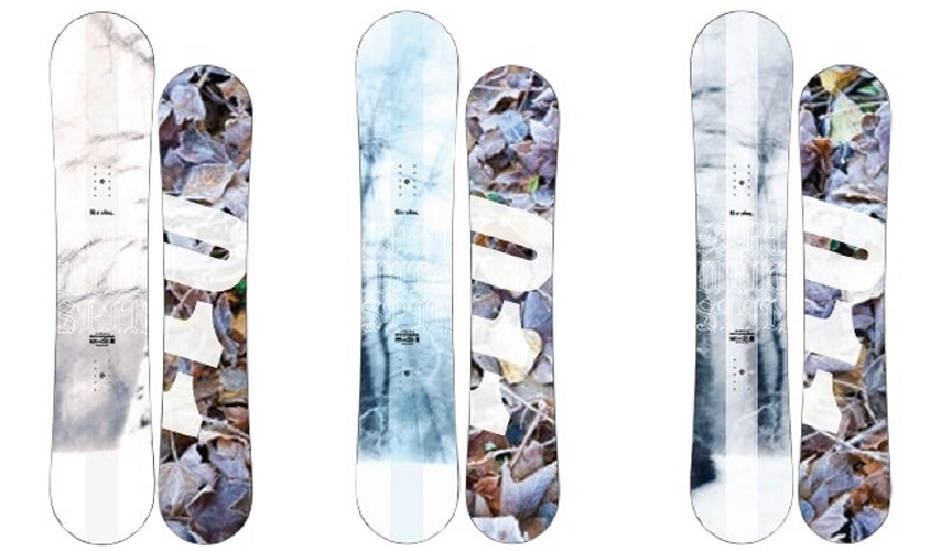 Three pairs of skis with abstract leaf-pattern artwork in white, blue, and brown tones, shown standing upright side by side (informative product image).