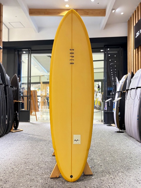 Yellow surfboard on a wooden stand, displayed upright in a shop surrounded by other boards.