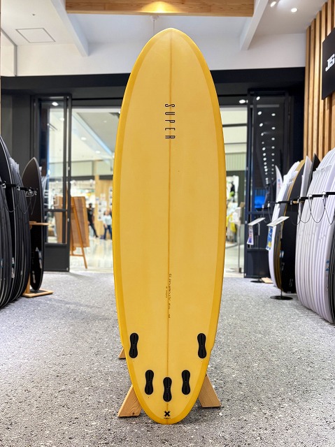 Yellow surfboard standing upright on a wooden stand in a surf shop, with other boards on display in the background.