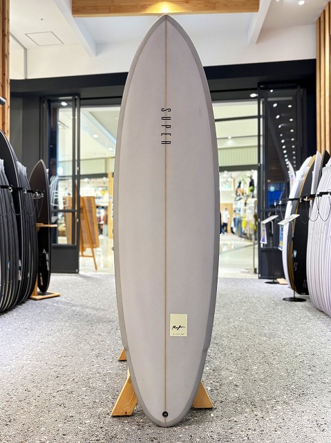 White surfboard on a wooden stand in a surf shop, with other boards on display in the background.