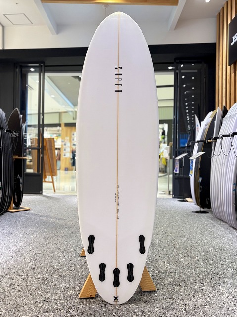White surfboard on a display stand inside a surf shop, with other boards visible in the background.